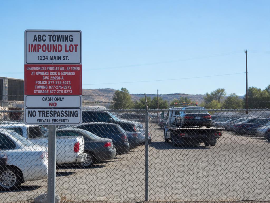 Private property impound lot with towed vehicles behind a chain link fence and signage